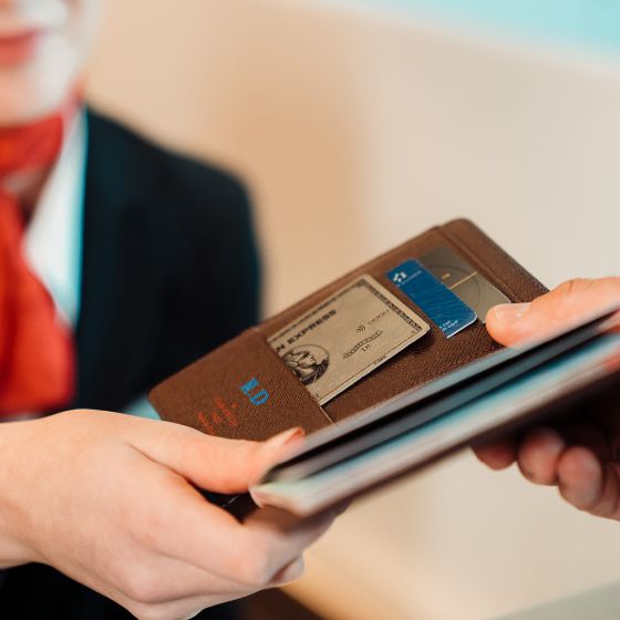 Nahaufnahme von zwei Händen, die eine American Express Platinum Card in einem Etui halten, im Hintergrund verschwommen eine Flugbegleiterin 