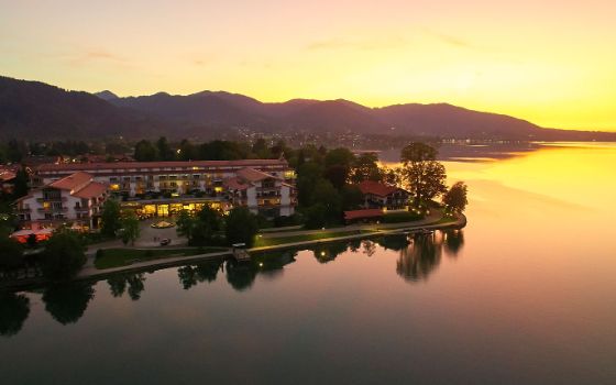 Ein luxuriöser Hotelkomplex am Seeufer vor Hügelkette bei Sonnenuntergang. 