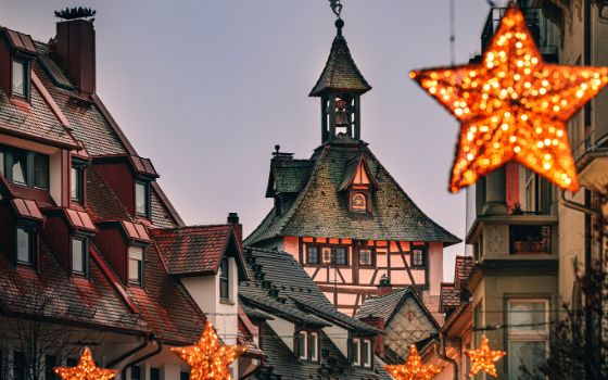 Glockenturm mit Fachwerkfassade in einer mit sternförmigen Lampen geschmückten Strasse einer Altstadt am Abend. 