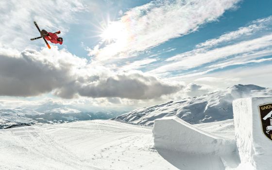 Ein Skifahrer bei einem Sprung in der Luft auf einem Parcours in einem Snowpark vor Gipfelpanorama.