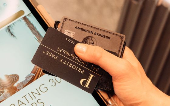 Eine Priority Pass Karte über einer American Express Platinum Card in der Hand einer Person. 