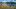 Seepanorama mit Nadelwald hinter blühenden Pflanzen im Vordergrund. 