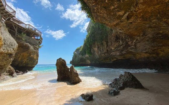 Ein Sandstrand mit blauem Meer ist umgeben von hohen Felsen und Klippen.