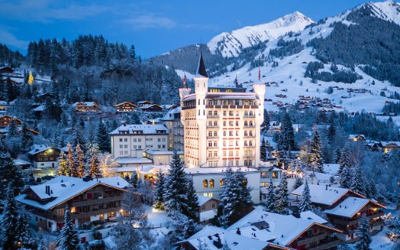 Beleuchtetes, schlossähnliches Hotelresort mit Steintürmen in verschneiter Berglandschaft bei Abenddämmerung.