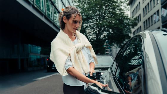 Eine Frau öffnet die Tür zu einem edlen Auto und hat dabei ein Smartphone in der Hand.
