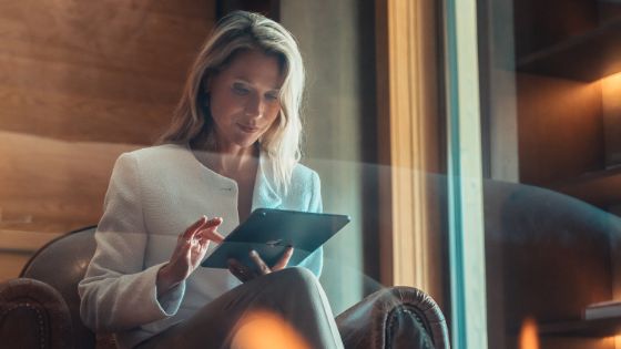 Eine Frau mit blondem Haar und weissem Blazer tippt auf einem Tablet.