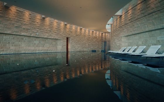 Ein lang gezogener Pool zwischen gemauerten Wänden, am Rand stehen weisse Liegen in einer Reihe.