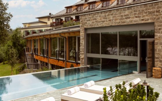 Gebäudekomplex mit einem schmalen Pool, der sich vom Inneren auf eine Terrasse mit Sonnenliegen zieht.