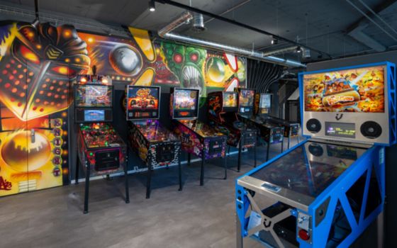 Ein Raum mit mehreren Flipperautomaten vor einer bunten Graffiti-Wand.