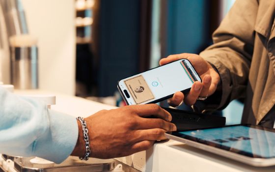 Ein Mann bezahlt bargeldlos mit seinem Smartphone, auf dem die goldene Kreditkarte von American Express aufleuchtet.