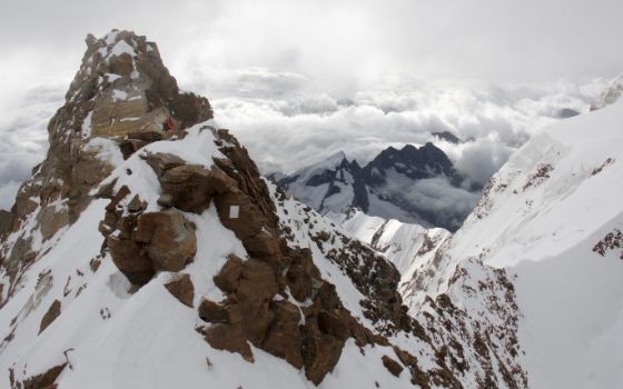Schroffe Felsspitze im Wallis mit Bergsteigern im Schnee – Blick über die Alpen und dramatische Wolkenkulisse