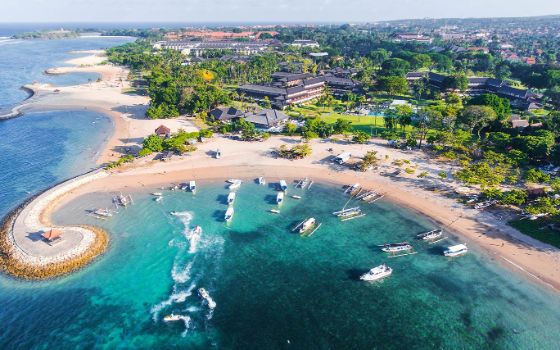 Luftaufnahme von vier kleinen Buchten mit Sandstrand blauem Meer, auf denen Boote schwimmen.