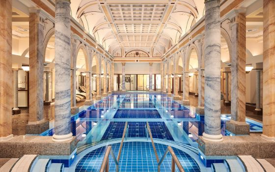 Prunkvolles Thermalbad mit Marmorsäulen und einem langen Pool mit blauem Kachelmuster.