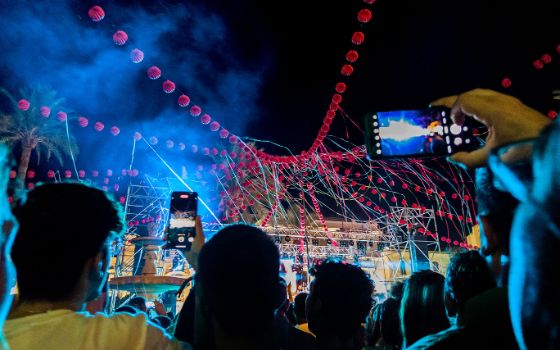 Personen stehen vor der Bühne eines Festivals und halten ihre Smartphones hoch. 