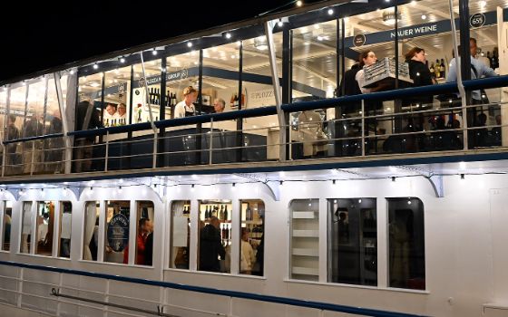 Seitenansicht eines beleuchteten Schiffes mit Personen an Weinbars an Ober- und Unterdeckbei Nacht. 