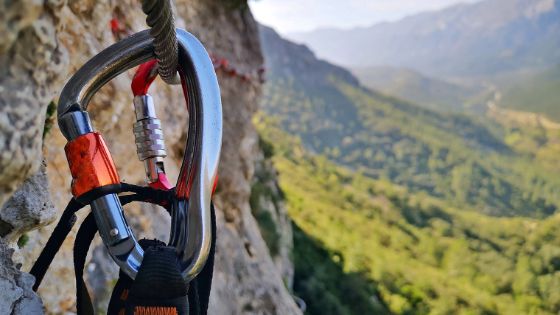 Ein Karabinerhaken hängt an einem Seil an in einer Berglandschaft. 