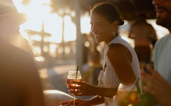 Eine Frau sitzt am Strand und hält ein Getränk in der Hand.