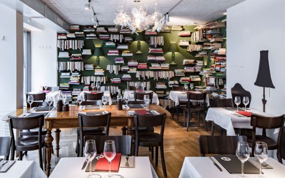 In einem Restaurant stehen gedeckte Tische und Stühle vor einer Wand mit vielen Büchern.