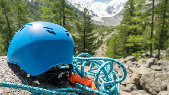 Ein blauer Helm liegt mit Seilen auf einem Stein, im Hintergrund ist eine bergige Waldlandschaft. 