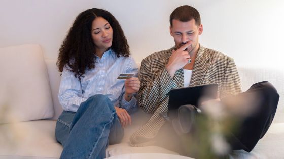 Eine Frau und einMann sitzen mit einem Laptop auf dem Sofa, sie hält eine Kreditkarte in der Hand. 