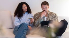 Eine Frau und einMann sitzen mit einem Laptop auf dem Sofa, sie hält eine Kreditkarte in der Hand. 