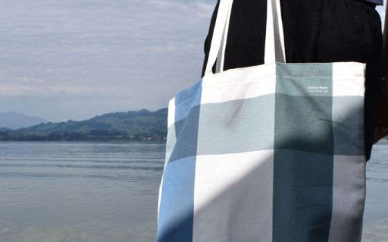 Ausschnitt von einer Stofftasche der Designerin Caroline Flueler, im Hintergrund sieht man einen See und Landschaft. 