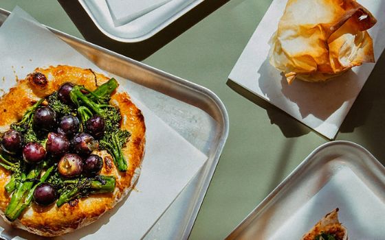Auf einer hellgrünen Tischplatte steht ein silbernes Blech, auf dem eine Pizza mit verschiedenen Arten von Gemüse liegt. 