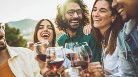 Vier Personen mit Weingläsern in der Hand lächeln sich an, es scheint, als würden sie sich über eine Sache freuen. 