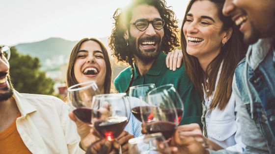 Vier Personen mit Weingläsern in der Hand lächeln sich an, es scheint, als würden sie sich über eine Sache freuen. 