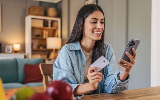 Eine Frau hält eine Kreditkarte in der Hand und schaut auf ihr Smartphone. 