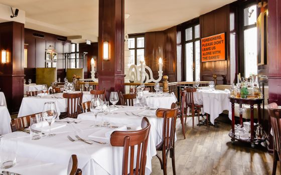 Heller Speisesaal mit Holzverkleidung und Holzstühlen an weiss eingedeckten Tischen.