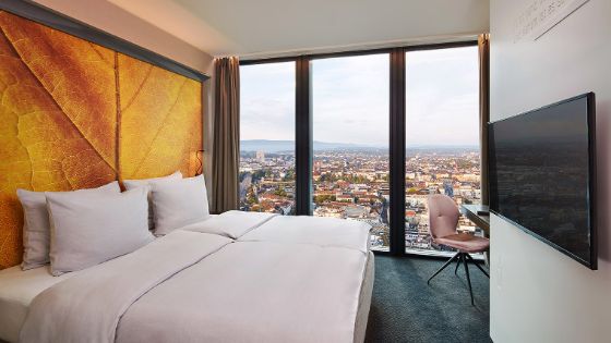 Modernes Hotelzimmer mit Doppelbett vor bodentiefem Panoramafenster mit Blick über Basel.