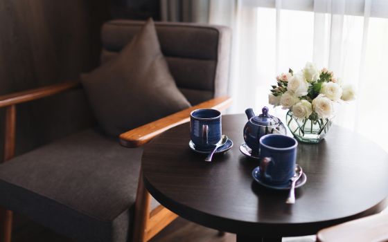 Ein eleganter Loungestuhl steht neben einem schwarzen Beistelltisch, auf dem zwei dunkelblaue Tassen und eine helle Blumenvase platziert sind.