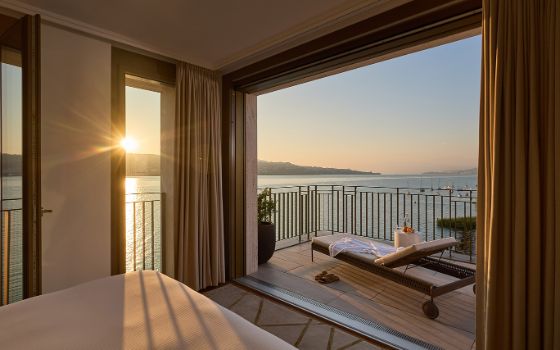 Ein Hotelzimmer hat eine Terrasse mit Sonnenliege und Blick auf einen See. 