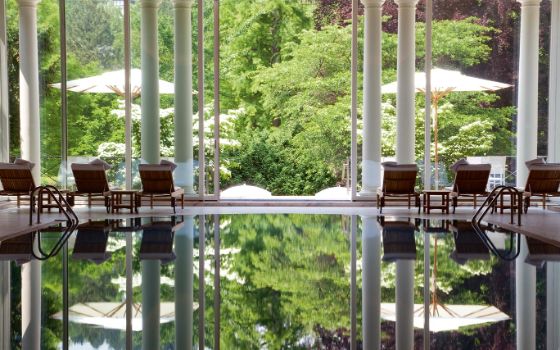 In einem Spa mit gläsernen Wänden stehen Liegen um einen Indoor-Pool.