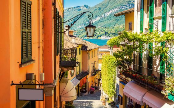 Gasse mit Treppenstufen in einem mediterranen Ort mit bunten Hausfassaden, im Hintergrund ein See vor Bergpanorama