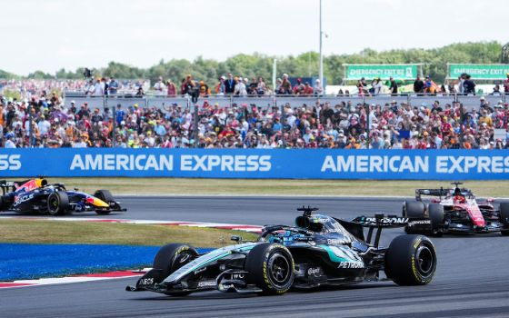 Ein dunkles «Formel 1»-Rennauto fährt in eine Kurve einer Rennstrecke, gefolgt von zwei weiteren Rennautos.