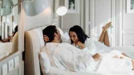 Paar entspannt im luxuriösen Hotelbett, trägt Bademäntel, geniesst romantischen Aufenthalt mit American Express Vorteilen