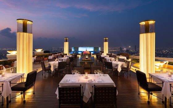 Auf einer Dachterrasse stehen gedeckte Tische umgeben von grossen Lichtern.