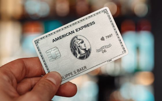 Nahaufnahme einer platinfarbenen Kreditkarte von American Express, die von einer Hand gehalten wird, der Hintergrund ist verschwommen.