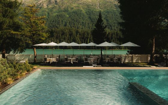 Aussenpool auf einer Terrasse mit Tischen, umgeben von Wald in einer Berglandschaft an einem See.