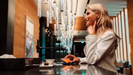 Eine elegante, lächelnde Frau mit einer American Express Platinum Card an der Theke in einem Foyer