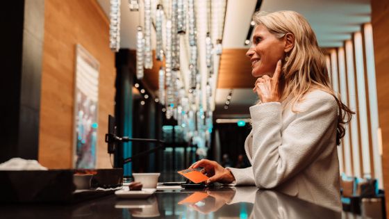 Eine elegante, lächelnde Frau mit einer American Express Platinum Card an der Theke in einem Foyer