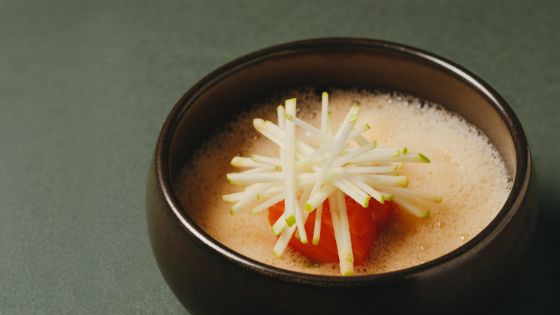 In einer braunen Schale ist ein Stück Lachs auf hellem Rübenpüree platziert und mit Gemüsestreifen garniert.