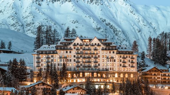 Beleuchtetes Grandhotel vor schneebedecktem Berg bei Abenddämmerung.