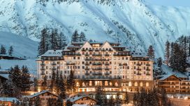 Beleuchtetes Grandhotel vor schneebedecktem Berg bei Abenddämmerung.