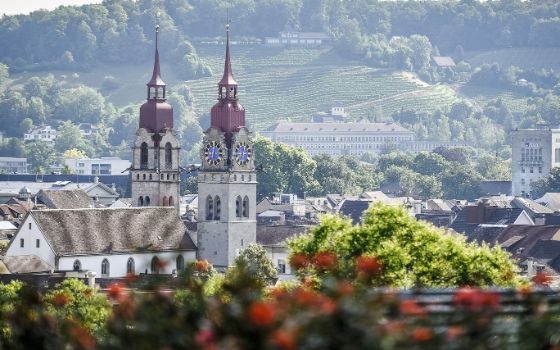 Die Stadtkirche Winterthur mit ihren zwei Türmen vor Weinbergen und Hügeln im Hintergrund.