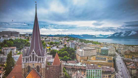 Historische Gebäude in Lausanne mit Kathedrale und Alpenpanorama im Hintergrund bei Abendlicht.