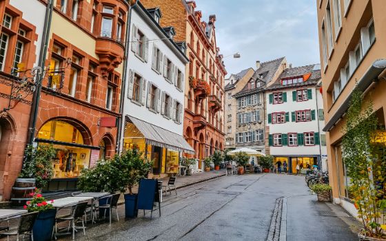 Farbenfrohe Gassen der Altstadt Basel mit historischen Häuserfassaden, Boutiquen und gemütlichen Strassencafés bei bewölktem Himmel.