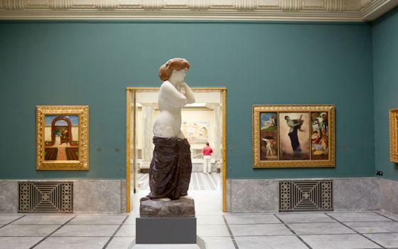 Ausstellungsraum in einem Museum mit Gemälden in goldenen Rahmen und einer Frauenstatue im Zentrum.